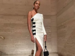Here’s How to Nail a White-Tie Dress Code (and Avoid All the Common Mistakes) Woman posing in a white one-shoulder maxi dress with black bows and a high leg slit.