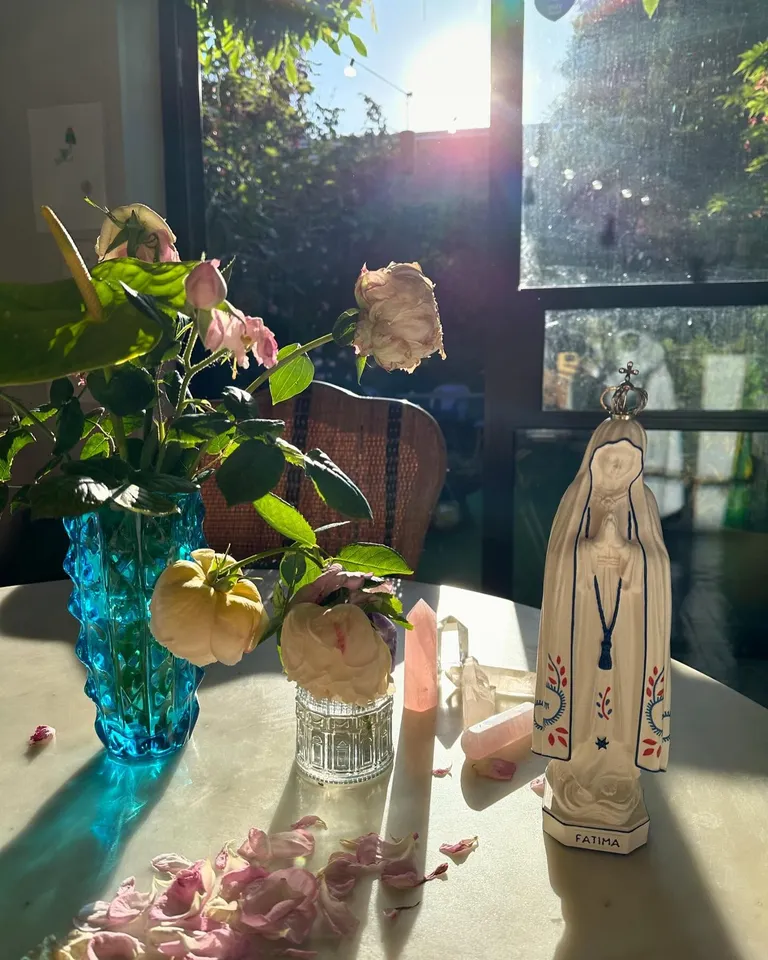 Sunlit table with pink roses, glass vases, crystals, and decorative figurine.
